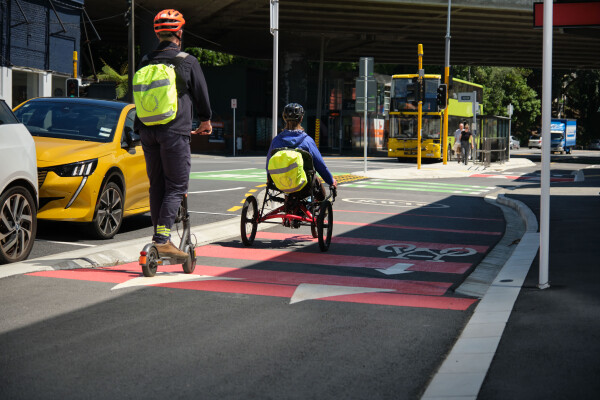 A scooter and a tricyclist with high-vis bag covers riding down a cycle lane