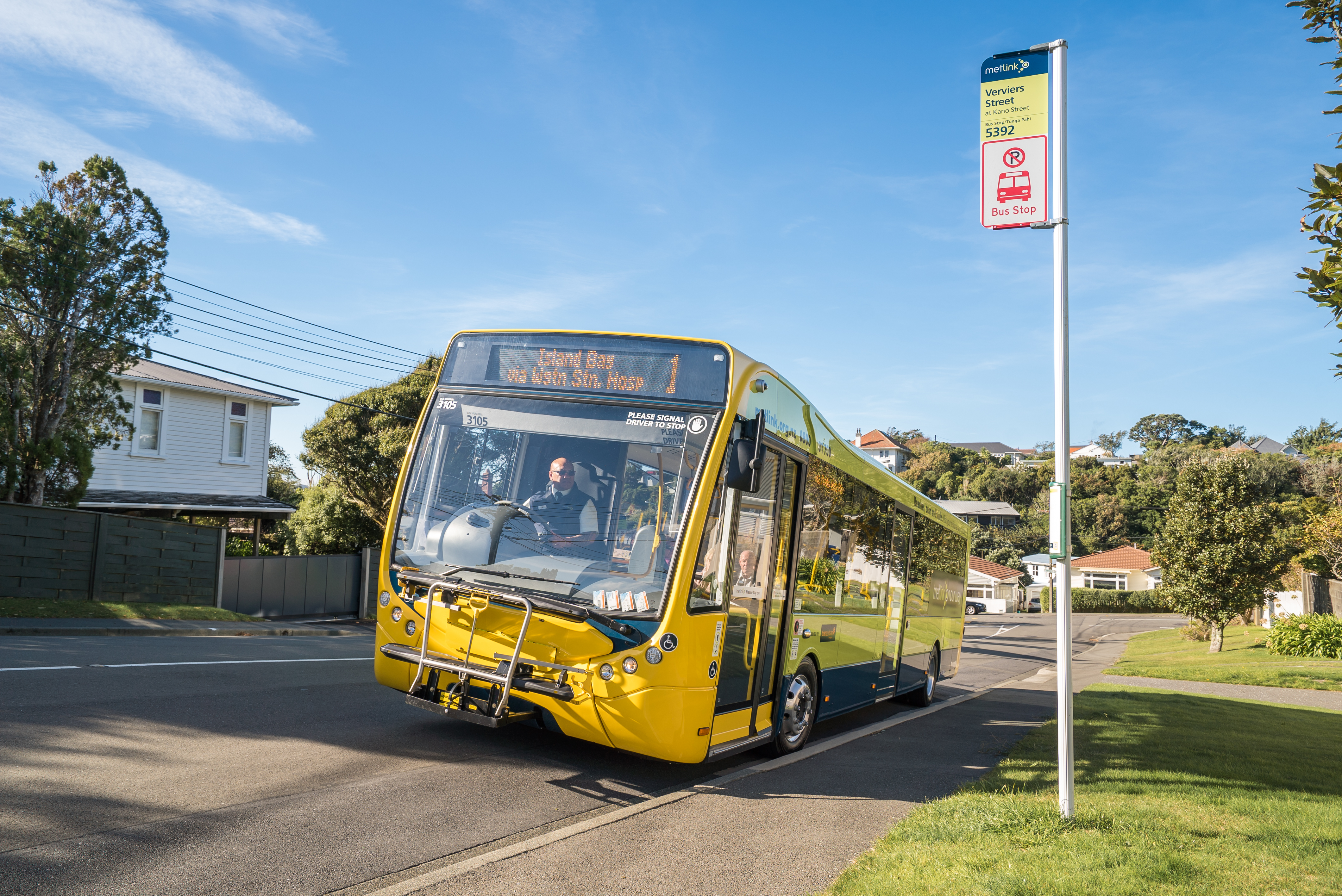 A bus pulling up to a bus stop on a sunny day