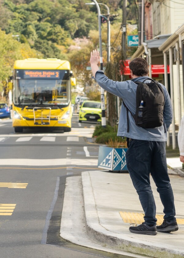 A person at a bus stop with their hand raised to signal to the bus driver
