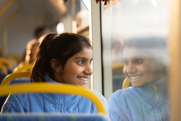 A smiling person looking out the window of a bus