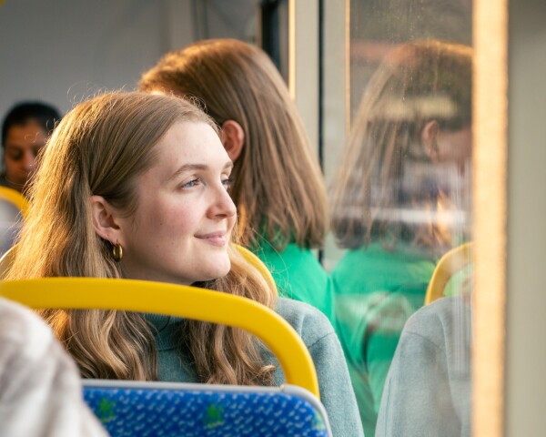 A smiling person looking out the window of a bus