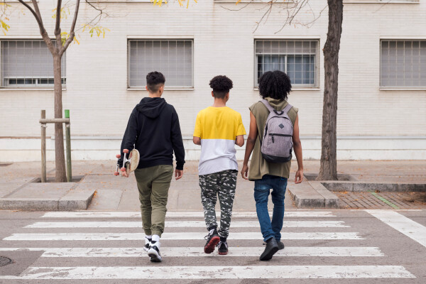 A view from behind three teenagers as they cross a road at a zebra crossing