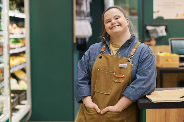 A woman in a work apron smiles at the camera