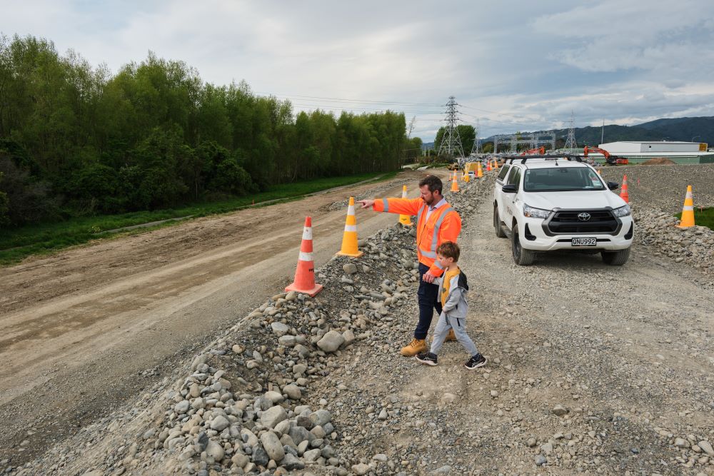 A man in hi-vis holds hands with a child and points at something on the Mills St Stopbank site