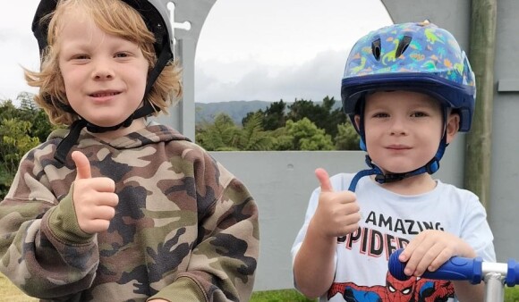Two students from Kelson School with helmets and scooters, smiling and giving the camera a thumbs up