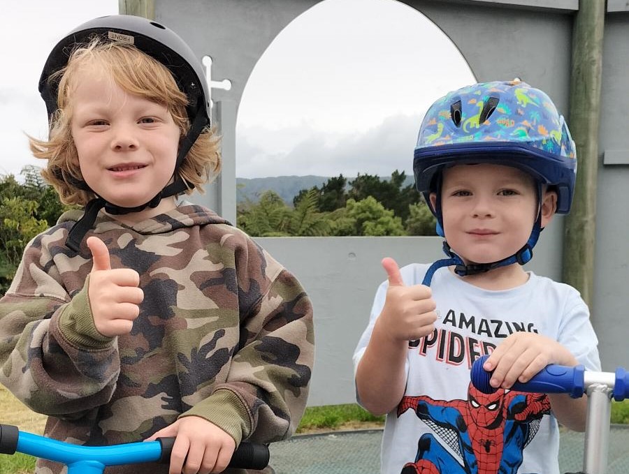 Two students from Kelson School with helmets and scooters, smiling and giving the camera a thumbs up