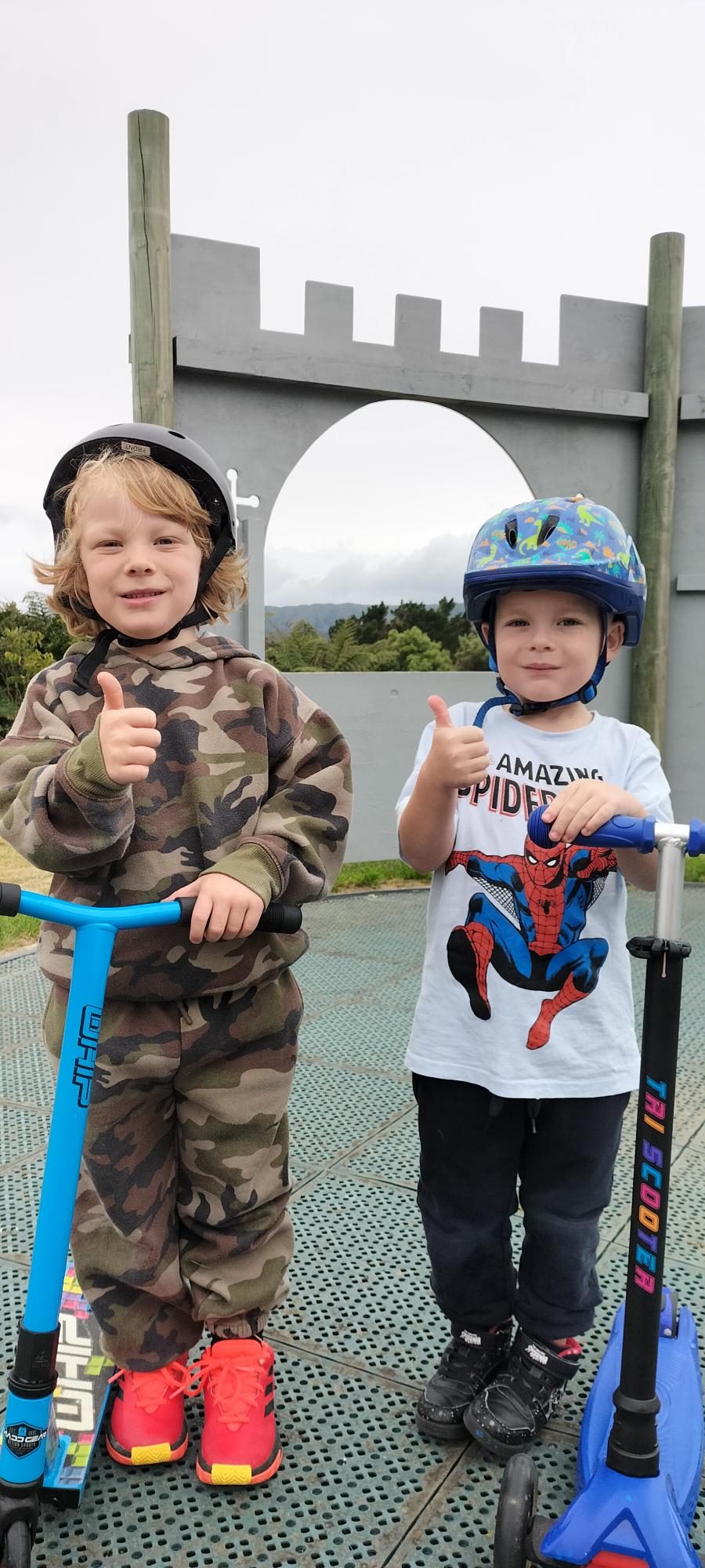 Two students from Kelson School with helmets and scooters, smiling and giving the camera a thumbs up